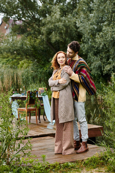 A man and a woman, dressed in boho-style clothing, stand on a dock by a serene lake.