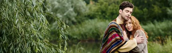 stock image A man tenderly holds a woman wrapped in a blanket amidst a romantic date in a green park.