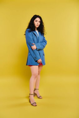 A young brunette woman with curly hair poses stylishly in front of a vibrant yellow backdrop, exuding a range of emotions. clipart