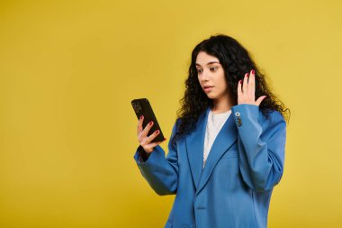 Mavi takım elbiseli esmer bir kadın cep telefonunu elinde tutuyor ve modern iletişimi gösteriyor..