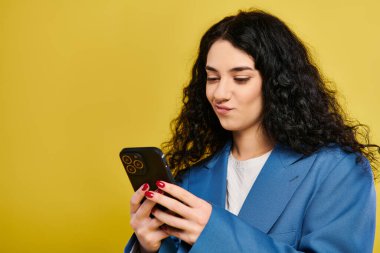 Mavi ceketli, kıvırcık saçlı, şık bir genç kadın sarı arka planda cep telefonuyla emilmiş..