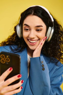 Kıvırcık saçlı, kulaklık takan ve müzik ve iletişim dünyasına dalmış bir cep telefonuna bakan genç bir kadın..