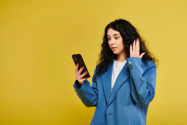 青いスーツの若いブルネットの女性は自信を持って携帯電話を保持し 現代のコミュニケーションを示しています — ストック写真
