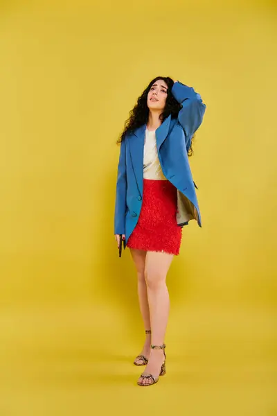 stock image A young, curly-haired brunette woman strikes a pose in stylish attire, showcasing her emotions against a vibrant yellow backdrop.