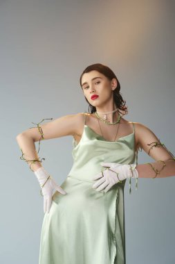 A young and beautiful woman with red lips poses gracefully in a green dress and white gloves in a studio setting on a grey backdrop. clipart