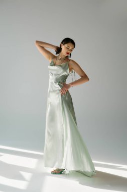 Kırmızı dudaklı genç, güzel bir kadın beyaz bir elbise içinde poz veriyor ve stüdyo ortamında eldiven takıyor. Nemf gibi bir aura yayıyor..