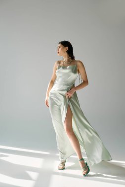 Kırmızı dudaklı genç, güzel bir kadın, uzun bir elbise ve gri arka planda bir stüdyoda eldiven giyiyor..