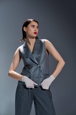 A stylish young woman strikes a pose in a gray suit with a vest, complemented by white gloves, set against a grey background. clipart