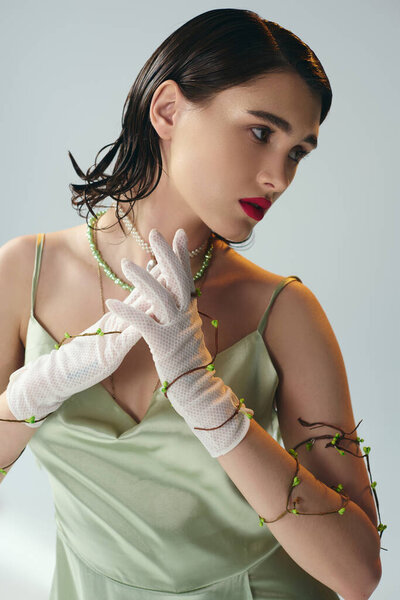 A young, beautiful woman with red lips poses in an elegant green dress and white gloves in a studio setting.