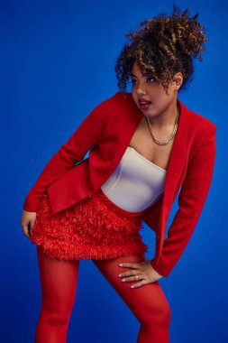 Çekici Afro-Amerikan modacıları şık ve şık kıyafetleriyle mavi arka plana bakıyorlar.