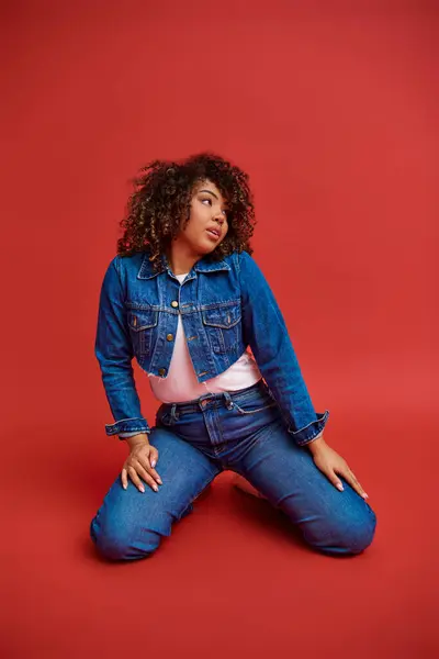 Привлекательная Молодая Африканская Американка Стильной Джинсовой Одежде Смотрящая Красный Фон — стоковое фото