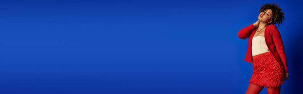 well dressed african american fashionista in elegant outfit looking away on blue backdrop, banner