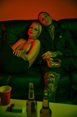 Bir adam ve bir kadın çılgın bir partide ya da gece kulübünde kanepede birlikte oturuyorlar.