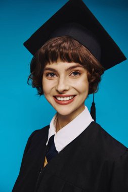 Siyahi mezuniyet elbisesi ve mavi arka planda akademik şapkalı gülümseyen üniversiteli kızın portresi.