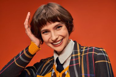 happy college girl with short hair posing in her uniform on orange background, high school clipart