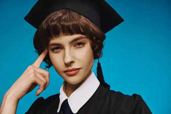 Portret Zamyślonej Studentki Czarnej Sukni Dyplomowej Akademickiej Czapce Niebieskim Tle — Zdjęcie stockowe