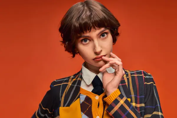 stock image student with short hair posing in stylish checkered blazer on orange background, college girl