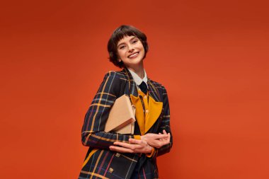 portrait of happy student in college uniform standing with books on orange background, knowledge clipart