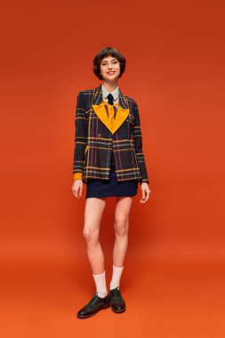 full length of college girl in checkered blazer and footwear with socks posing on orange backdrop clipart