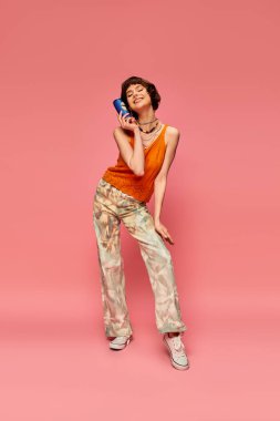 Kısa esmer saçlı kaygısız genç kadın pembe yaz içeceği üzerinde poz verirken elinde soda kutusu tutuyordu.