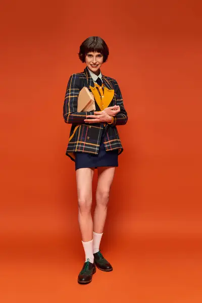 Portret Pozytywnego Studenta Uniformie Koledżu Stojącego Książkami Pomarańczowym Tle Wiedza — Zdjęcie stockowe