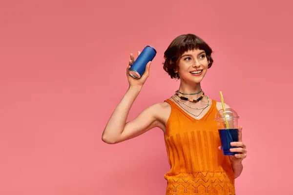 ピンクの背景に夏の飲み物を保持し 短いブルネットの髪とピアスを持つ喜ばしい若い女性 — ストック写真