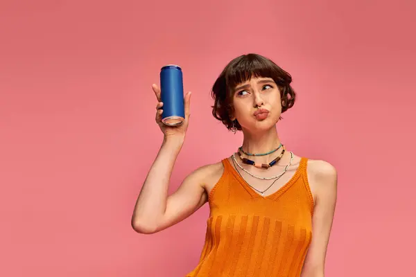 stock image uncertain young woman with short brunette hair and piercing holding soda can on pink, summer drink