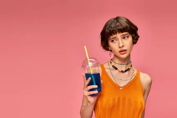 ピンクの背景にさわやかな夏の飲み物を保持する短いブルネット髪の不満の若い女性 — ストック写真