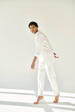 Zarif, çekici Afro-Amerikan adam rahat bir şekilde bej arka planda poz veriyor ve kameraya bakıyor.