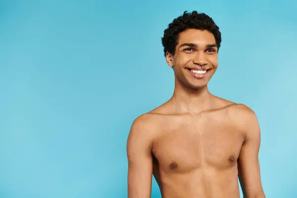 stock image cheerful handsome african american man in blue swimming trunks looking away on blue backdrop