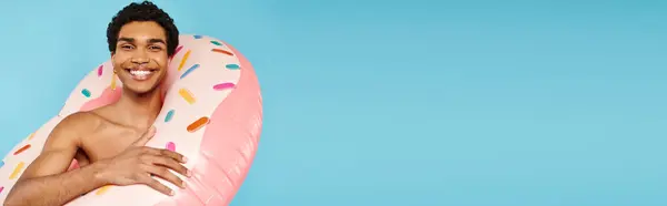 stock image merry african american man posing with swimming ring on blue backdrop and looking at camera, banner