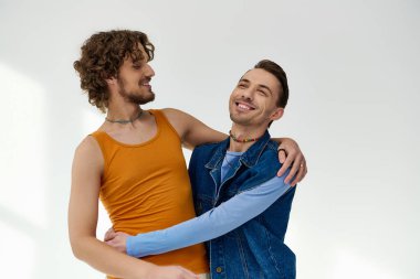 Güzel görünümlü, neşeli Igbtq arkadaşları canlı giysiler içinde gri arka planda sarılıyorlar, gurur ayı