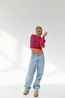 Beyaz şapkalı neşeli gay adam gri arka planda poz veriyor ve kameraya bakıyor.