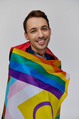Neşeli, neşeli, rahat giyinen, elinde gökkuşağı bayrağı tutan ve kameraya gülümseyen bir gay.