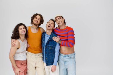 Gri arka planda poz verirken kameraya gülümseyen canlı giyinmiş dört çekici gay adam.