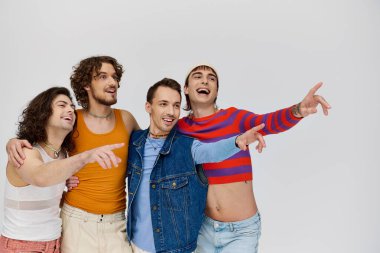 Gri arka planda birlikte poz veren ve başka yöne bakan neşeli lgbtq erkekleri cezbediyor