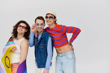 Neşeli, çekici, son moda güneş gözlüklü, elinde gökkuşağı bayrağı olan ve kameraya gülümseyen gay erkekler.