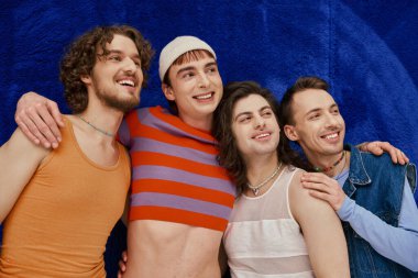Her gün mavi arka planda parlak giysiler içinde dört neşeli, çekici gay arkadaş, gurur ayı.