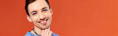 stylish joyous good looking gay man with stylish makeup posing with rainbow flag, pride month clipart