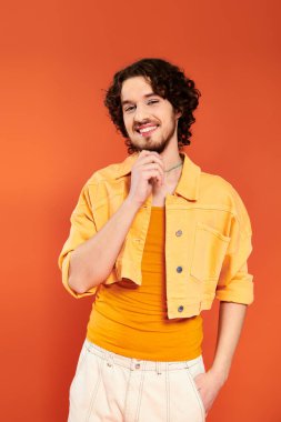 Turuncu arka planda poz veren koyu renk saçlı ve canlı makyajlı çekici eşcinsel adam, gurur ayı.