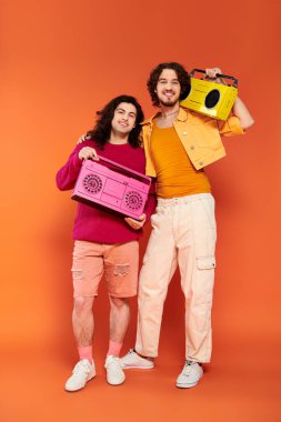 two joyous attractive gay friends in vibrant clothes posing with tape recorders, pride month clipart