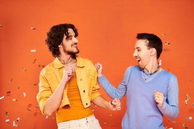 positive good looking gay friends in stylish clothes with makeup posing under confetti rain, pride clipart