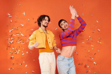 joyful good looking gay friends in stylish clothes with makeup posing under confetti rain, pride clipart