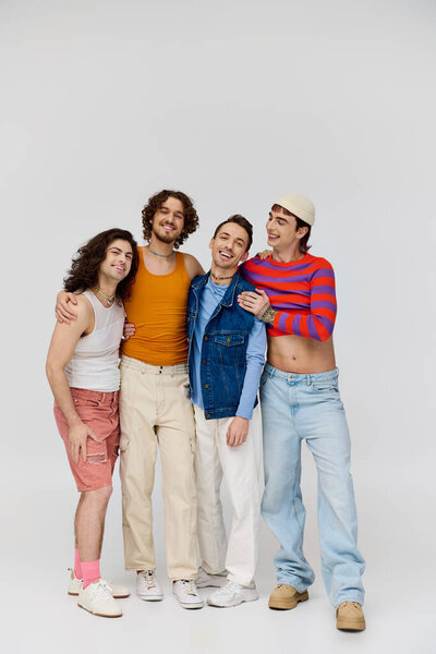 four merry good looking gay men in vivid attires smiling at camera while posing on gray backdrop