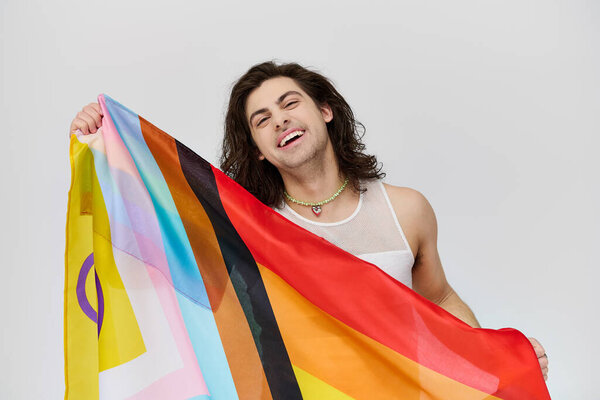 attractive joyous gay man with long dark hair posing with rainbow flag and looking at camera