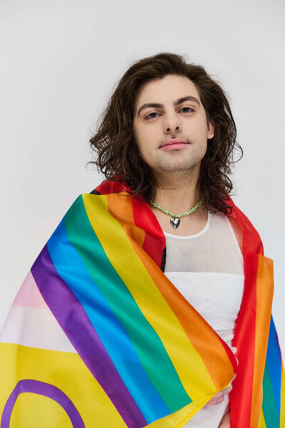 good looking joyous gay man with long dark hair posing with rainbow flag and looking at camera
