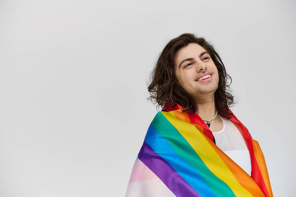 good looking fancy jolly gay man in vivid attire with rainbow flag looking away on gray backdrop