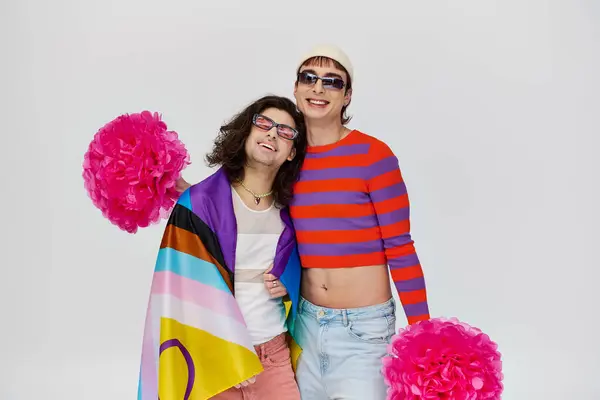 レインボーフラッグとポンポンとサングラスの大胆な服装で2人の陽気で魅力的なゲイ男性 — ストック写真