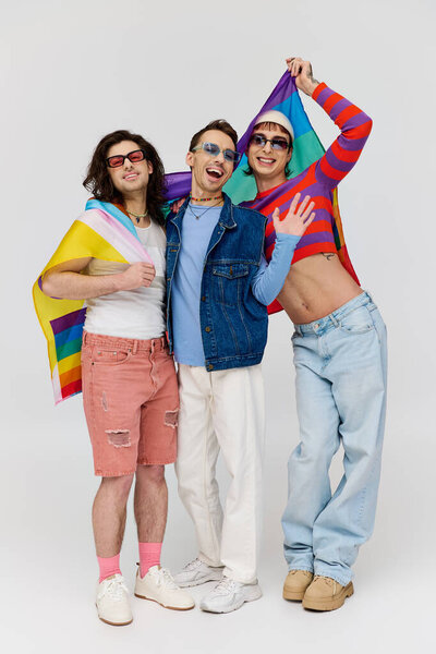 joyful appealing gay men with trendy sunglasses holding rainbow flag and smiling at camera