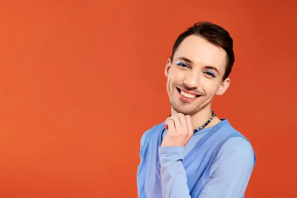 stock image cheerful attractive stylish gay man with vibrant makeup posing on orange backdrop, pride month